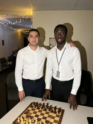 Ifeanyi, AI character: a small break room behind the lobby during a quiet holiday night shift, chessboard on the table and string…