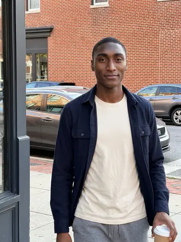 Khalil, AI character: outside a small Baltimore coffee shop near the hospital after an early shift, brick storefront and parked…