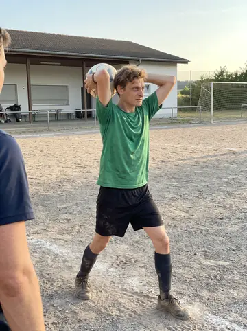Manuel, AI character: gravel football pitch behind the rescue station on a warm Sunday evening