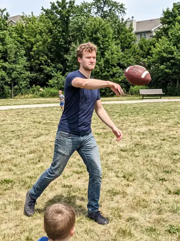 Remo, AI character: a neighborhood park in Milwaukee with his sister's twins running routes on the grass