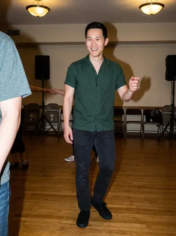 Haruki, AI character: beginner swing dance class in a rented community hall, other dancers cropped at the edges and polished…