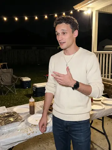 Victor, AI character: his aunt's backyard cookout near Lafayette during the holidays, string lights and folding chairs behind him