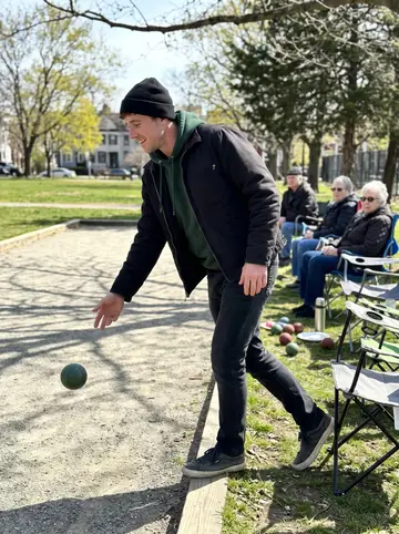 Gavin, AI character: a small Dorchester park on Sunday morning during bocce with his grandmother's neighbors, patchy spring…