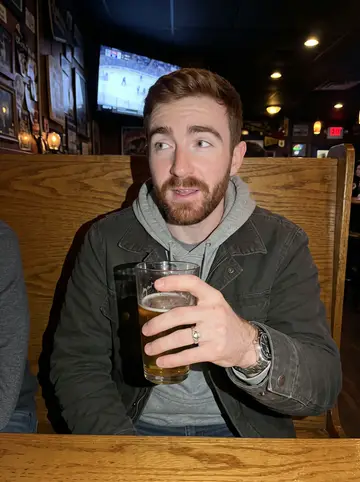 Cahir, AI character: a crowded Pittsburgh neighborhood bar during a Bruins game, wood booths and a TV glow behind him