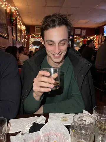 Corrado, AI character: a small Bensonhurst bar after a holiday shift swap, warm string lights and friends cropped at the edges