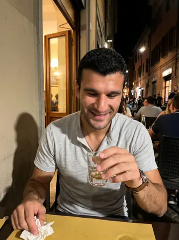 Ignazio, AI character: outside a small osteria in Bologna after a late shift, crowded tables and a dark street behind him
