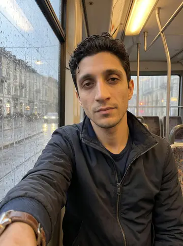 Stelvio, AI character: inside a Turin tram after work, rain-streaked window and blurred streetlights behind him