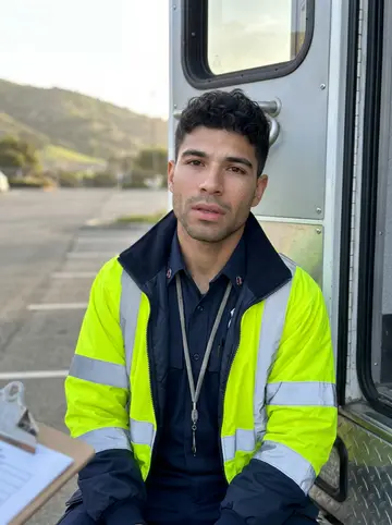 Thiago, AI character: the crew station parking lot in Redding, a folding chair on the asphalt, a crewmate seated in it with a…