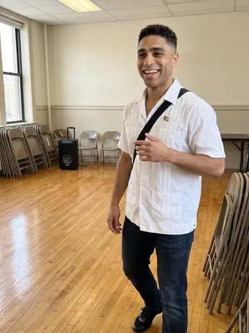 Isaac, AI character: a bright community center dance room in the Bronx after Sunday salsa class, polished wood floor and…