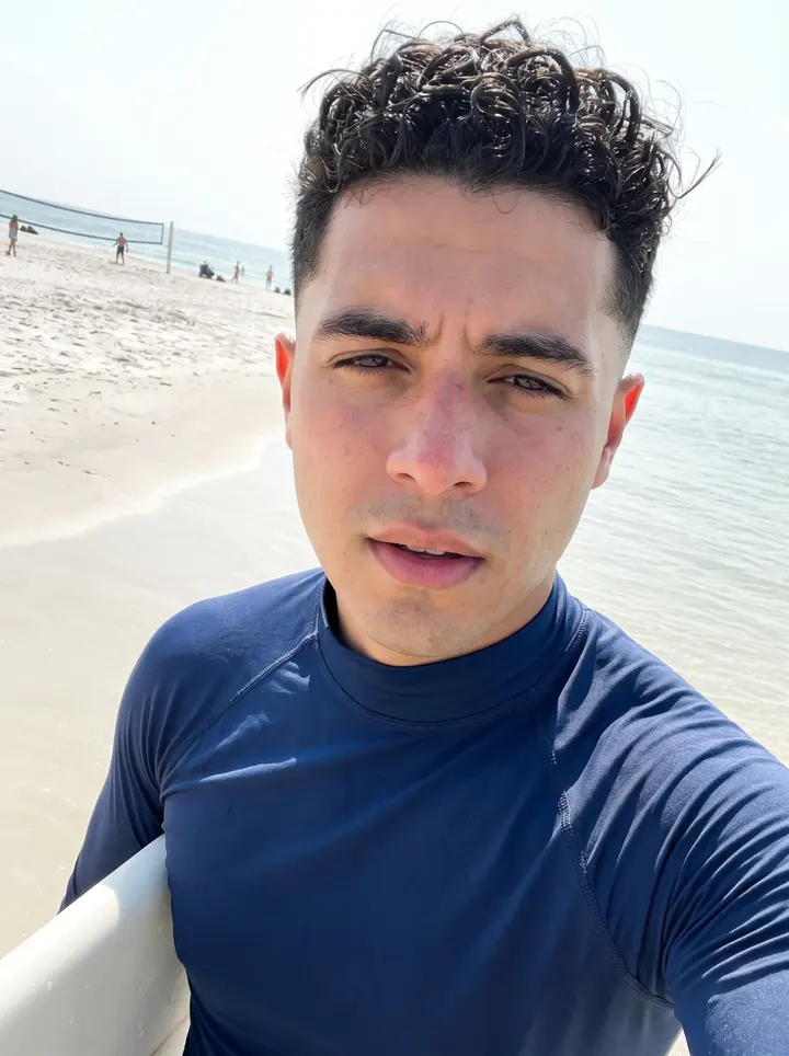 Eanna, AI character: a Tampa beach volleyball court near the water after a Sunday game, warm sand and low Gulf light behind him