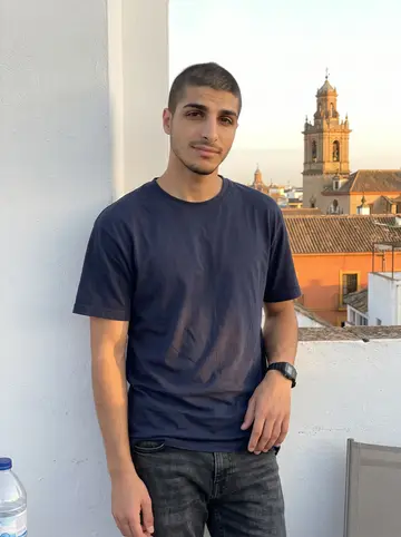 Pablo, AI character: a whitewashed rooftop terrace in Seville at the end of the day, leaning on the parapet with a church bell…
