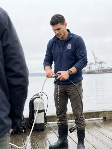 Tiago, AI character: the floating pontoon at the maritime police dive unit on the Tagus in Lisbon, a cargo crane and the grey…