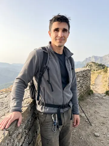 Anselmo, AI character: a stone lookout above Jaca with the Pyrenees behind him, late afternoon after a short climb