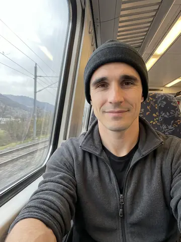 Anselmo, AI character: on a regional train after scouting streets in his new town, grey hills passing outside the window