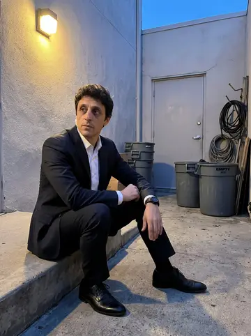 Bartolomé, AI character: a service entrance courtyard behind a Beverly Hills event venue during a quiet break between security sweeps