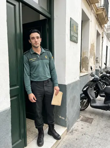 Sebastián, AI character: outside the Guardia Civil station in Cádiz during a quiet afternoon, green doorframe and parked scooters…