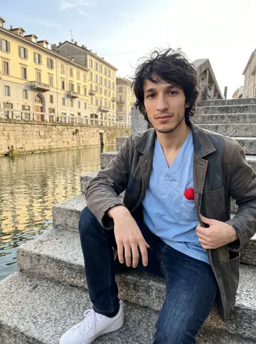 Davide, AI character: stone steps beside a quiet Milan canal after his early shift, with warm late sun on the buildings behind him