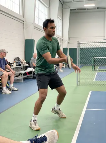 Nathan, AI character: Salem rec center pickleball court, painted green floor and chain-link divider behind him, older players…