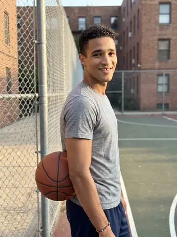 Kobby, AI character: the apartment basketball court in Philadelphia at golden hour, chain-link fence and brick apartment blocks…