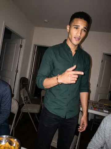 Kobby, AI character: apartment common room during a casual game night, folding chairs and snack bowls behind him