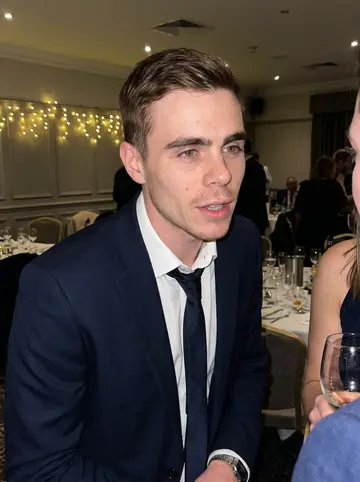 Callum, AI character: a cousin's wedding reception in a Yorkshire hotel function room, warm fairy lights and guests blurred…