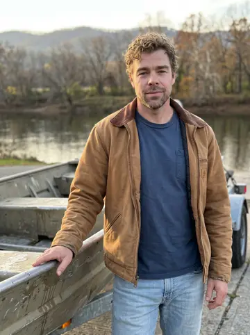 Abbott, AI character: the concrete boat ramp on the New River at dusk, leaning against his dented aluminum jon boat on its…
