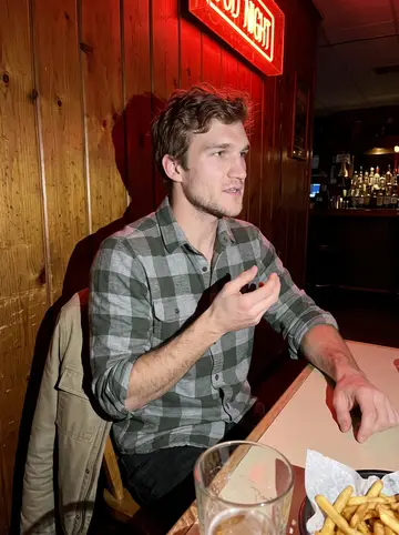 Corbin, AI character: a wood-paneled small-town bar in Salmon, Idaho, a pint glass and a basket of fries on the table in front…