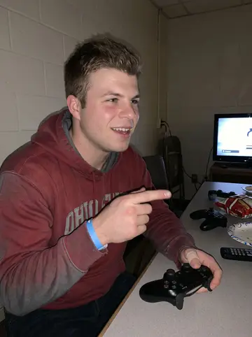 Paul, AI character: station dayroom on a slow Sunday night, Mario Kart paused on the TV behind him and controllers scattered…