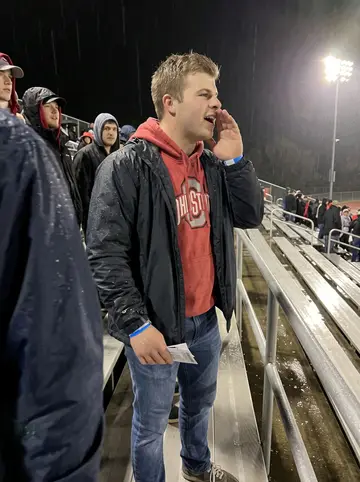 Paul, AI character: cheap metal bleachers at a Friday-night high school football game in Dayton, damp field lights glowing…