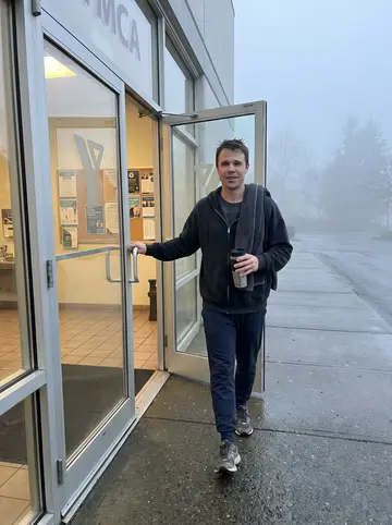 Sean, AI character: outside the YMCA before work, foggy early morning sidewalk, glass doors and old posters behind him