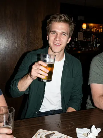 Cooper, AI character: a quiet neighborhood bar in Tacoma after shift with two coworkers cropped at the edges, dark wood wall behind