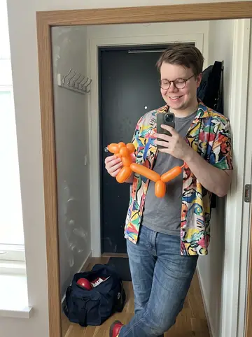 Jarrod, AI character: his apartment kitchen in Columbus, kitchen table crowded with balloon animals and a half-open gym bag…