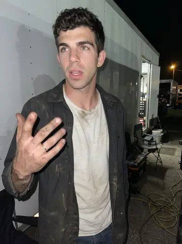 Conner, AI character: night rally paddock near the monster truck trailers, folding chairs and toolboxes behind him