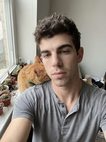 Conner, AI character: his apartment windowsill crowded with succulents labeled after bones, Femur the orange tabby pressed…