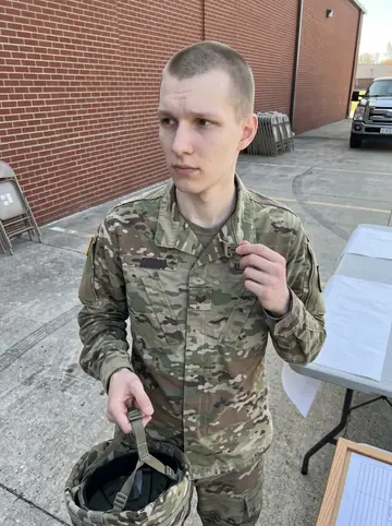 Bram, AI character: Ohio National Guard armory parking lot on a drill weekend, folding tables and a unit sign-up board near…