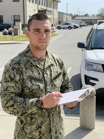 Leonard, AI character: outside the Camp Lejeune provost marshal office near a white patrol vehicle and concrete bollards