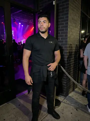 Wilhelm, AI character: outside a busy Austin nightclub entrance after midnight, velvet rope and dark brick wall behind him