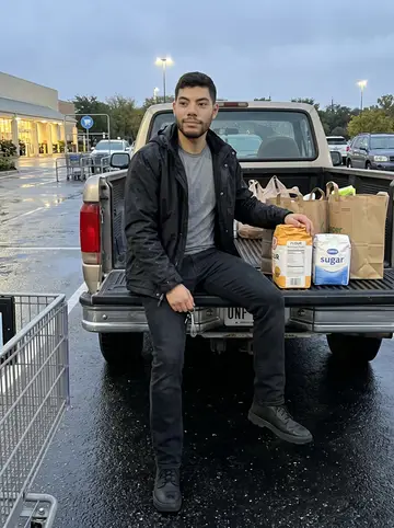 Wilhelm, AI character: a grocery store parking lot in Austin after buying cake supplies, wet asphalt and his old pickup behind him