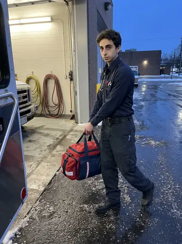 Branislav, AI character: the ambulance bay outside his Cleveland EMS station before a night shift, wet pavement and open bay door…