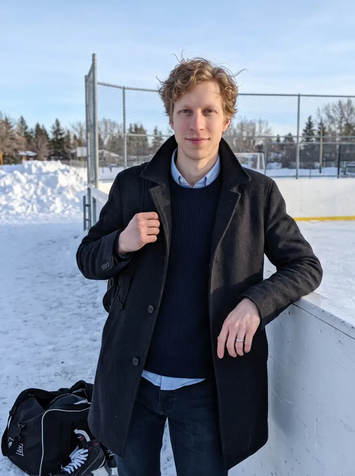Jiří, AI character: outside a community outdoor rink in Edmonton on a clear cold afternoon, leaning on the rink boards with…
