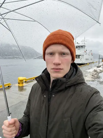 Magnus, AI character: the frozen Prestvannet lake on the edge of Tromsø, leaning against the side of his small hand-built red…