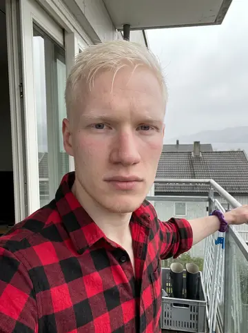 Magnus, AI character: his small apartment kitchen in Tromsø on a rainy spring evening, a window with rain streaks behind him, a…