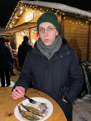 Jere, AI character: a crowded Christmas market food stall in Joensuu, paper plate of fried vendace and pickled herring on a…