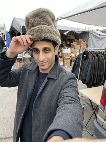Mazen, AI character: outside a plain brick police district building in Philadelphia after shift, wet sidewalk and parked cars…