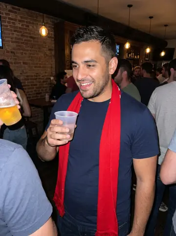 Goran, AI character: a crowded neighborhood bar in Chicago after a Fire soccer match, friends cropped around him