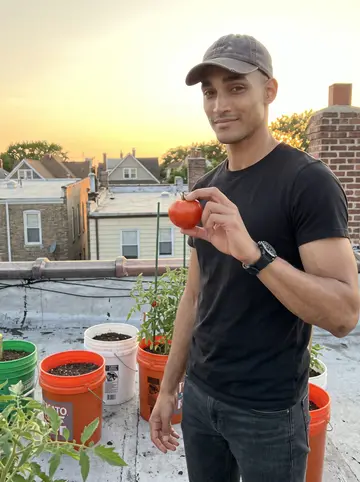 Rome, AI character: his mother's South Side two-flat roof with tomato buckets, brick chimneys, and warm evening sky behind him