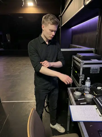 Ole, AI character: inside the nightclub before doors open, beside the sound desk and a clipboard of staff names