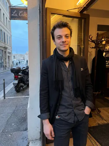Aurélien, AI character: outside La Cale in Marseille just before opening, standing in the narrow doorway under warm entrance…