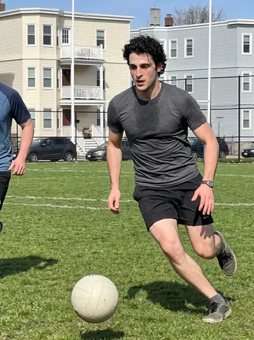 Kieran, AI character: a public grass field in Dorchester during Sunday-morning Gaelic football pickup, goalposts and…