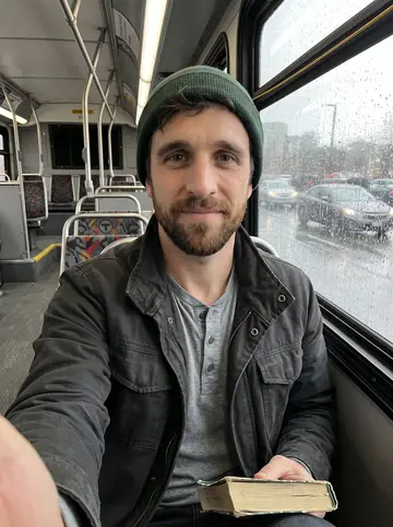 Barry, AI character: an MBTA bus seat on a rainy spring afternoon, wet windows and soft city traffic behind him